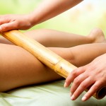 Hands massaging female legs with bamboo.
